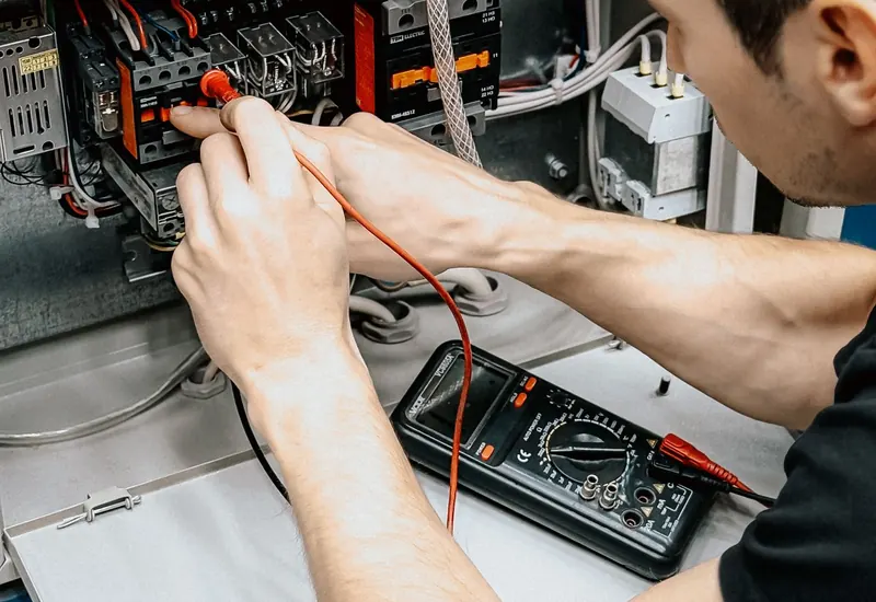 Electrician testing an open electrical panel with a multimeter